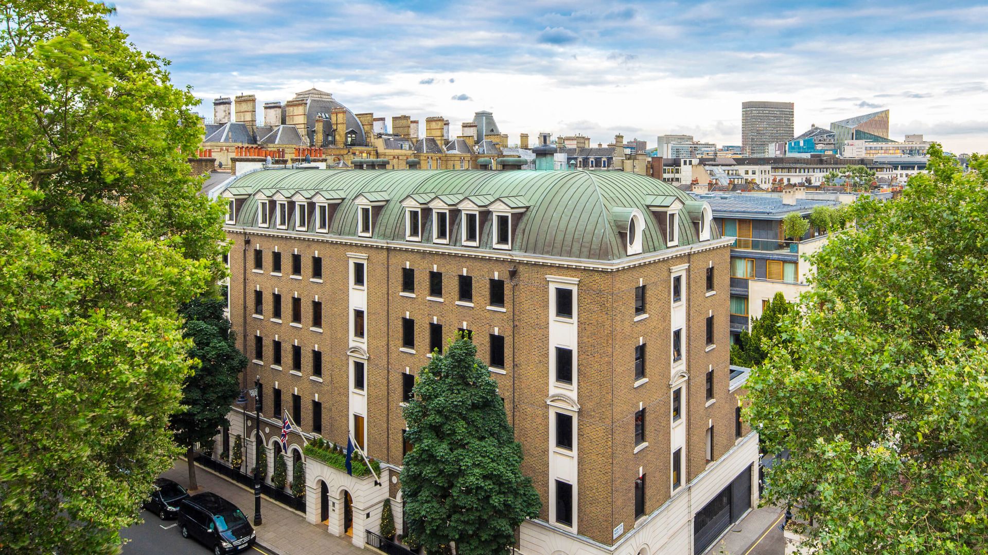 A Road With Cars And Trees By A Large Building