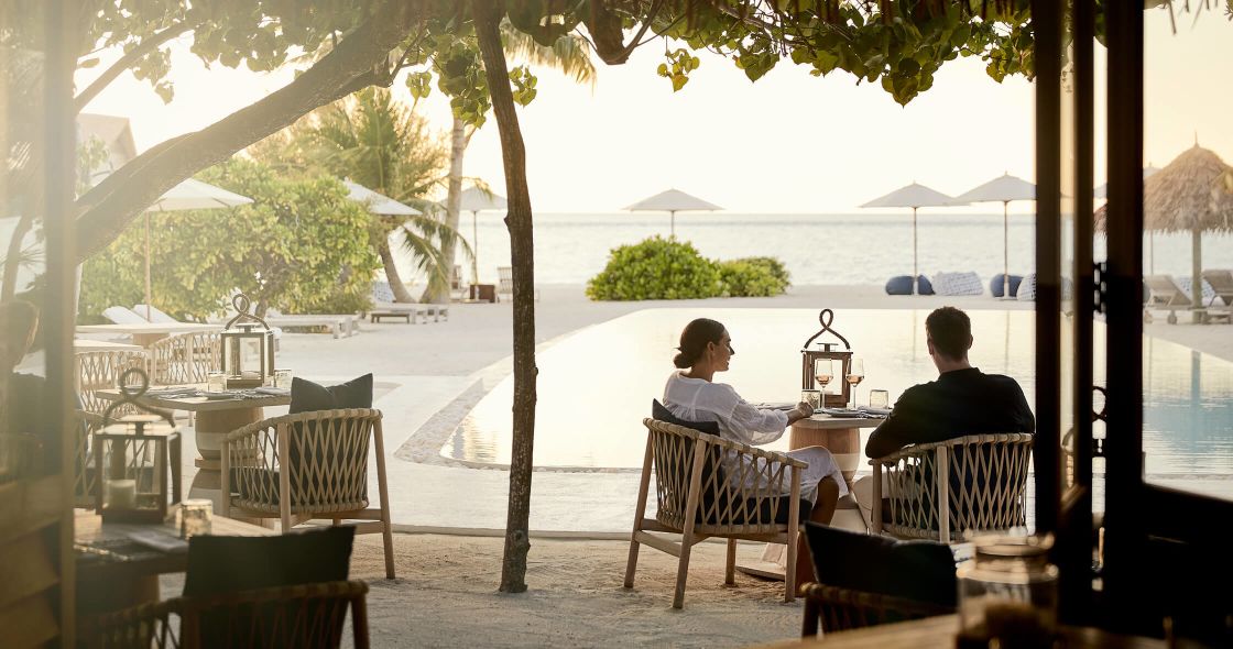 A Couple Of People Sitting At A Table Outside