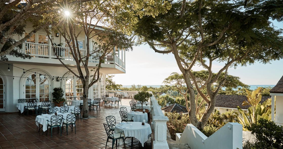 A Patio With Tables And Chairs And Trees And A Building In The Background