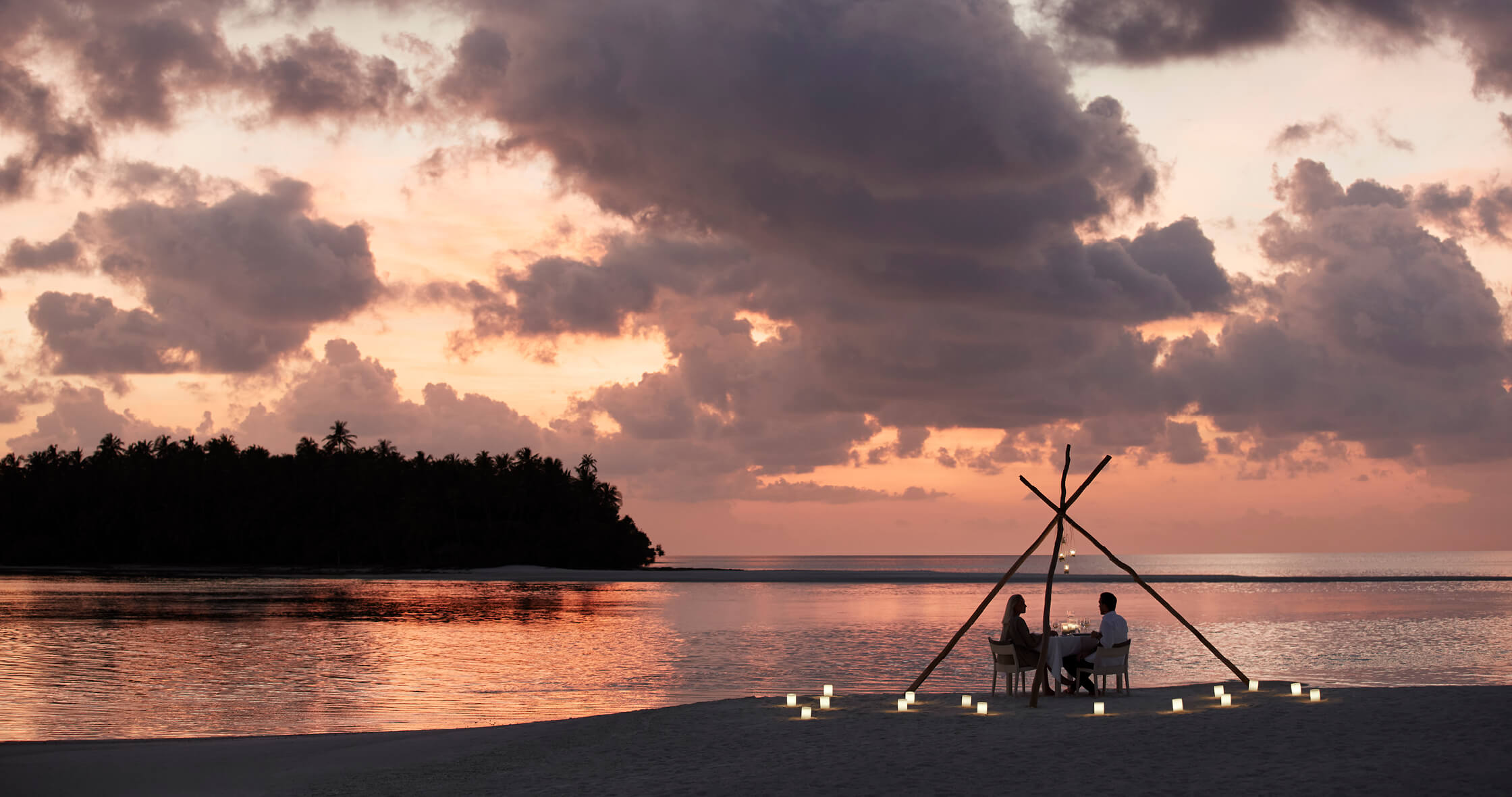 A Couple Sitting On A Chair By A Body Of Water