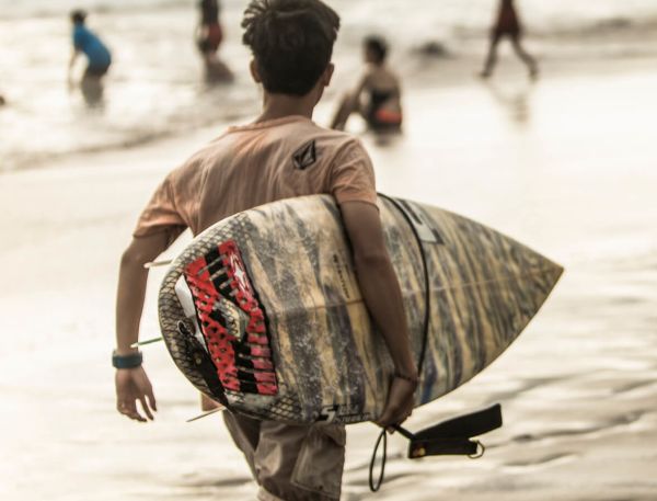 A Person Carrying A Surfboard On A Beach